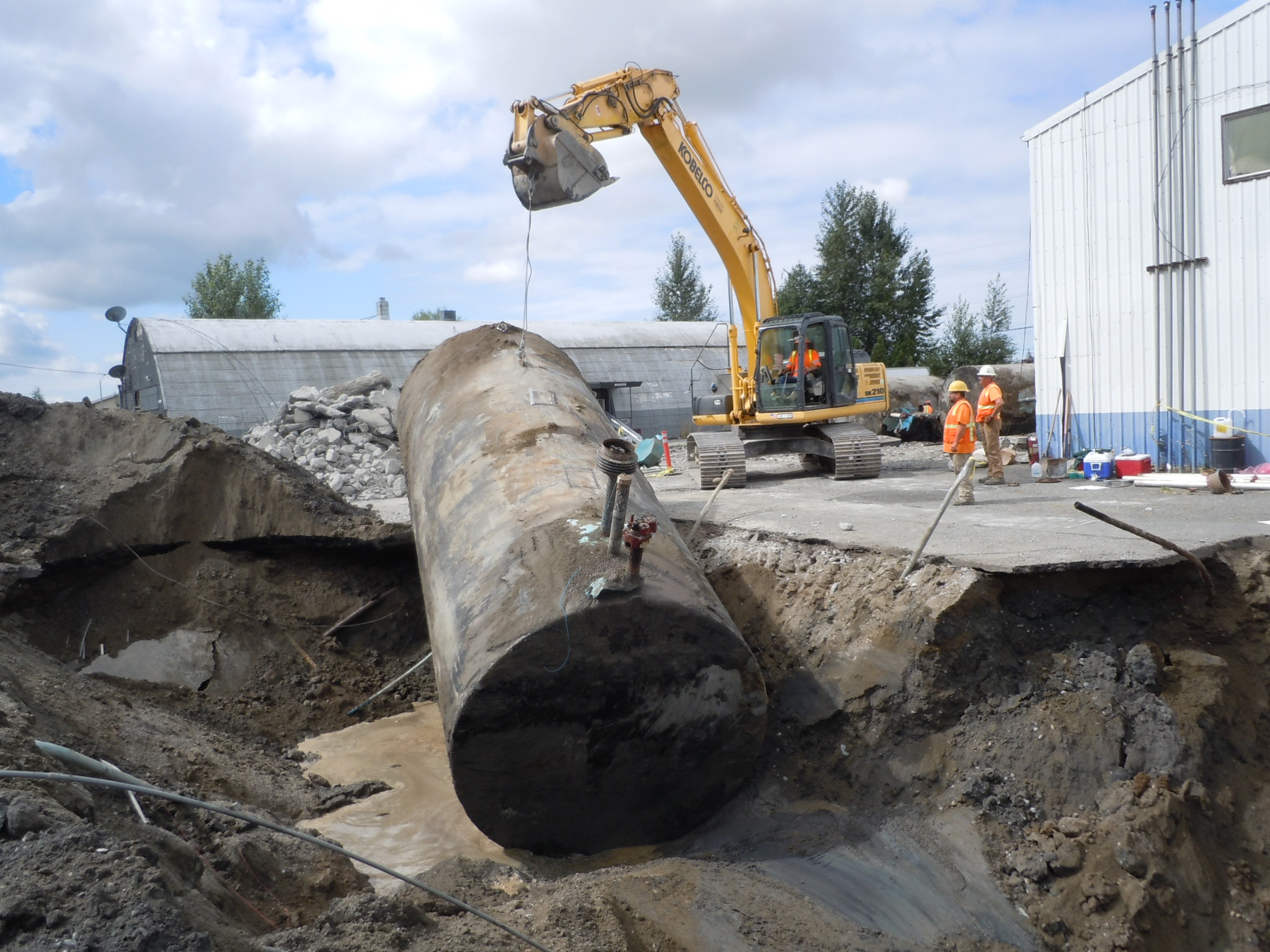 An excavator pulls an gas tank out of an excavation site. 