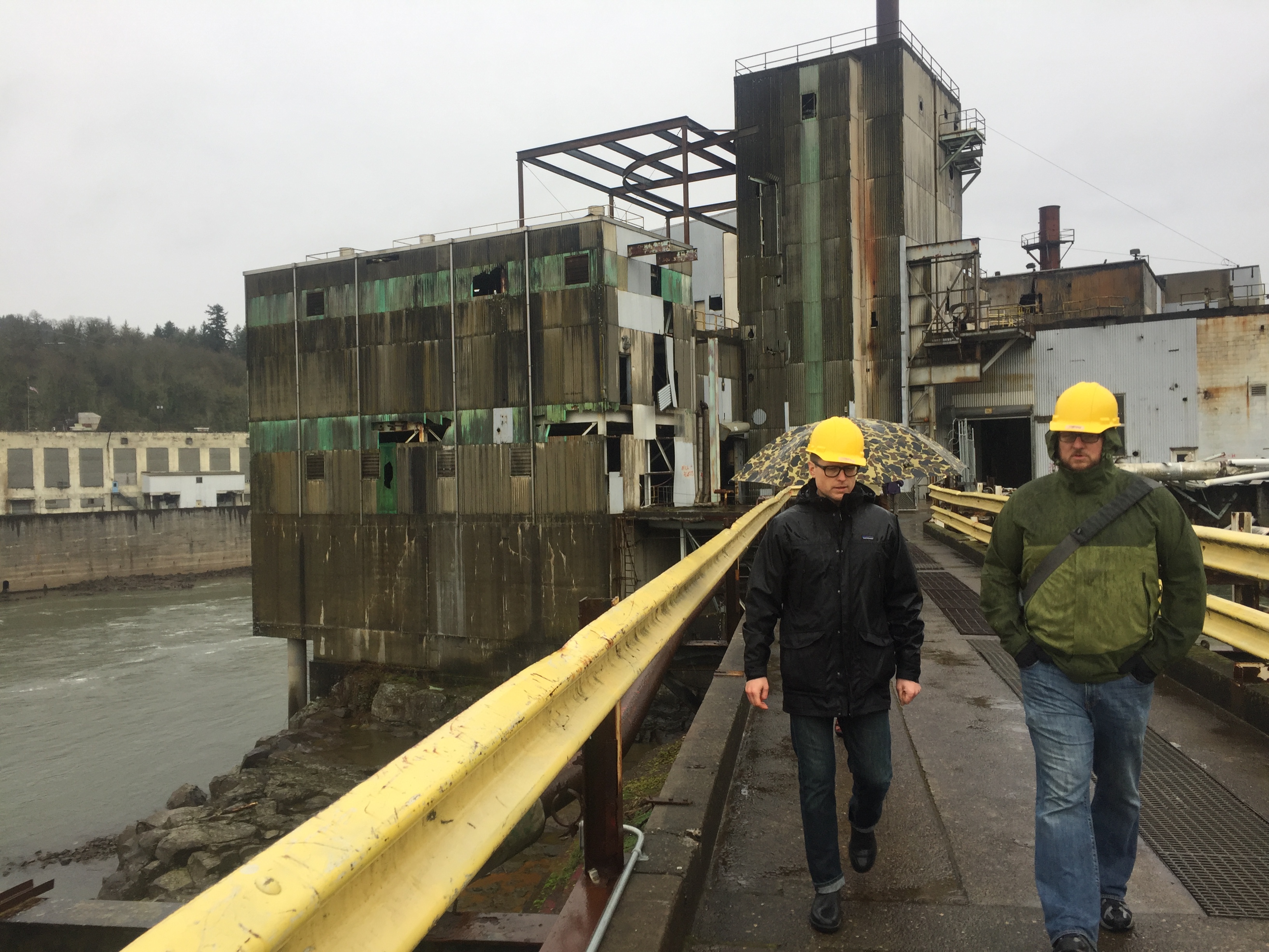 Two men wearing hard hats walking on a former industrial site.