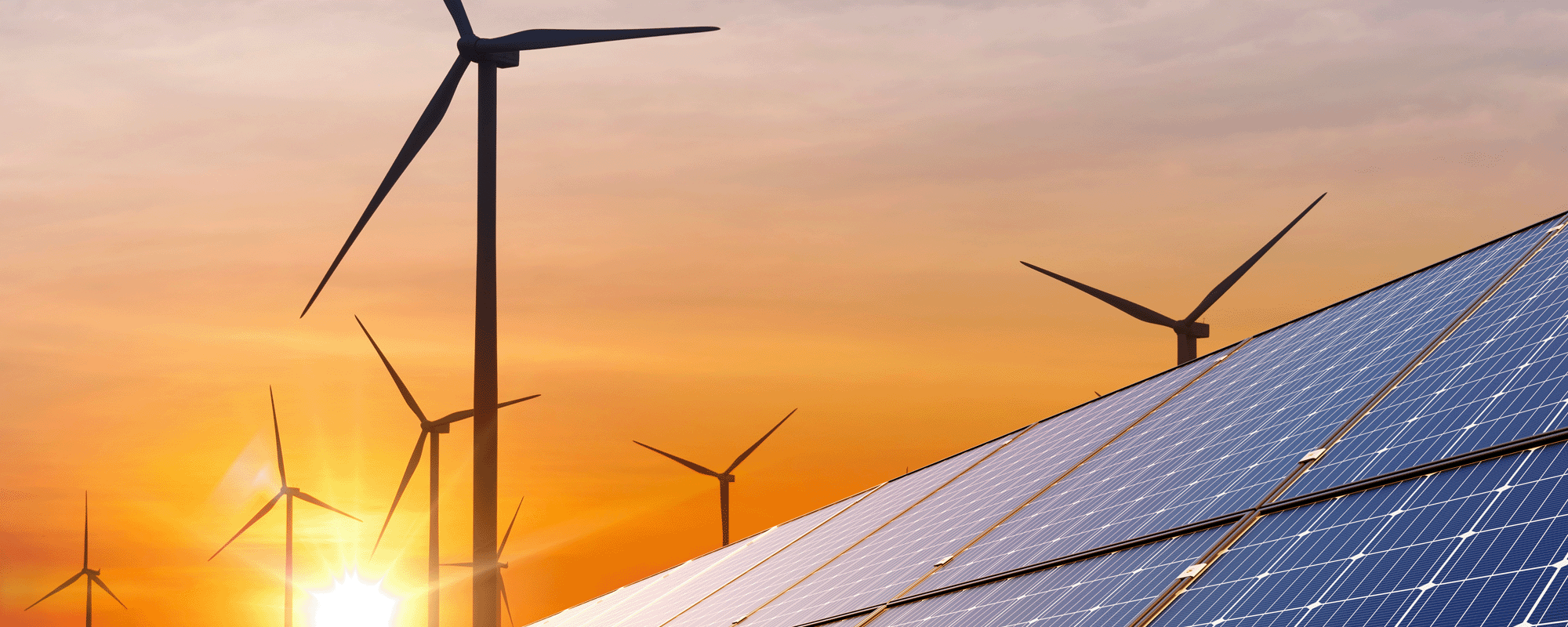 Solar panels and wind turbines generate energy at sunset, with the sun casting an orange glow over the scene.