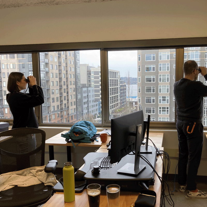 Two people looking out the window with binoculars.