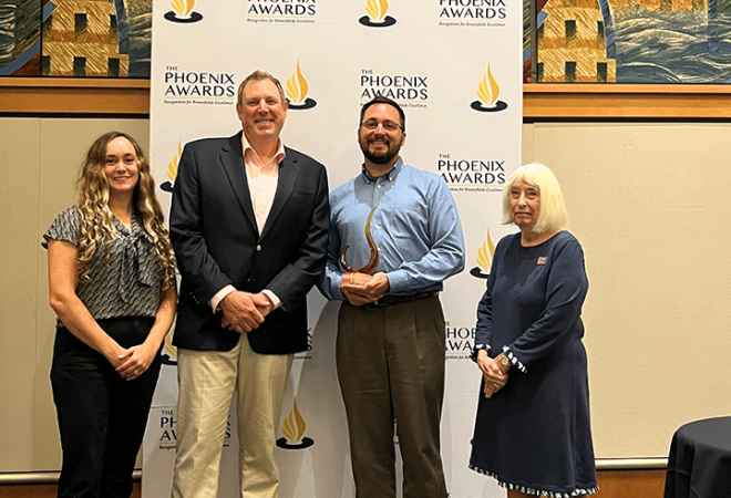 four people in front of award banner