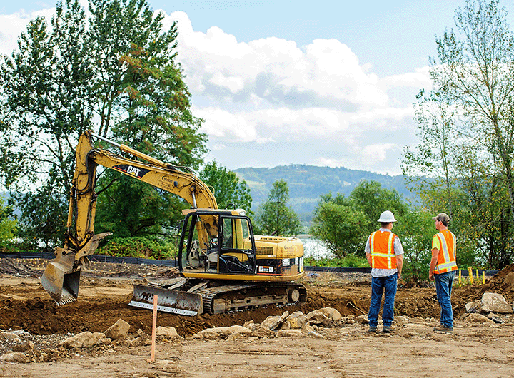 two workers in safety vests standing next to an excavator at the Washougal Waterfront Park project site