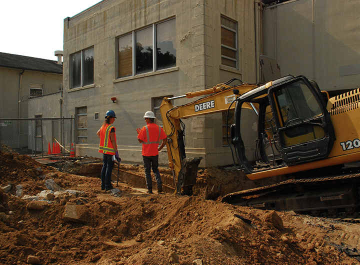 two construction workers standing near an excavator at a brownfield site