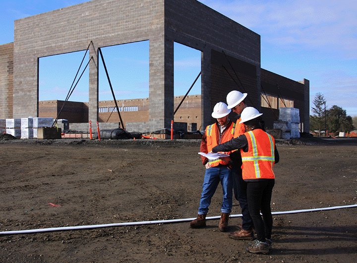 three workers in safety gear looking at documents at a project site